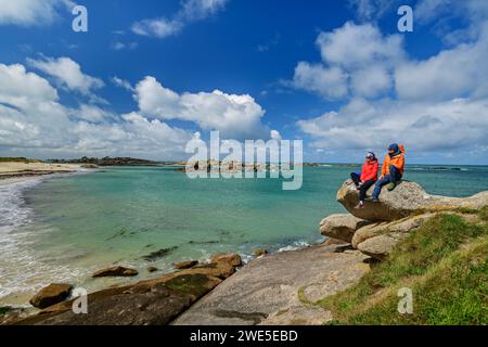 Mann und Frau wandern auf Felsen und blicken auf den Sandstrand, Trégastel, Côte de Granit Rose, Bretagne, Frankreich Stockfoto