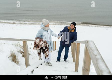 Ein älteres Paar klettert im Winter am Meer eine Holztreppe. Stockfoto