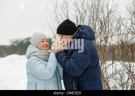 Ein älterer, fürsorglicher Mann wärmt seiner Frau auf der Straße mit dem Atem die Hände. Valentinstag Stockfoto