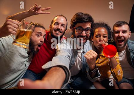 Selfie mit einer Gruppe von Freunden, die Fußballspiele im Fernsehen sehen, während sie nachts auf dem Sofa sitzen Stockfoto