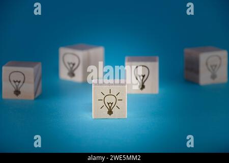 Mehrere Holzwürfel mit Glühbirnensymbolen auf tiefblauem Hintergrund, einer davon ist eingeschaltet und zeigt Brainstorming und Konzeptentwicklung. Stockfoto