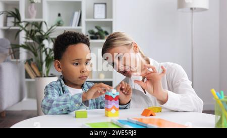 Beurteilung der psychischen Entwicklung von Kindern. Ein professioneller Psychologe beobachtet einen kleinen multirassischen Jungen, der mit einem Puzzlespiel spielt und seine bewertet Stockfoto