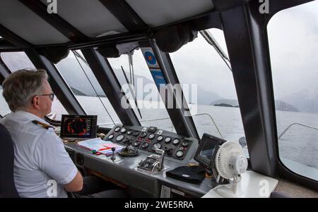 Schiffskapitän, der eine Passagierfähre mit Hilfe eines Simrad Autopiloten auf Lake Manapouri, Aotearoa (Neuseeland), Te Waipounamu (Südinsel) führt Stockfoto