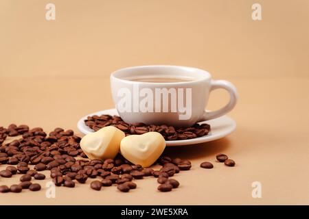 Kaffeetasse und Kaffeebohnen, herzförmige Bonbons und auf beigefarbenem Hintergrund. Valentinstag-Konzept. Nahaufnahme. Stockfoto