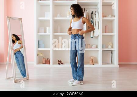 Eine Frau in Jeans runzt sich bei ihrem Spiegelbild, besorgt um das Gewicht Stockfoto