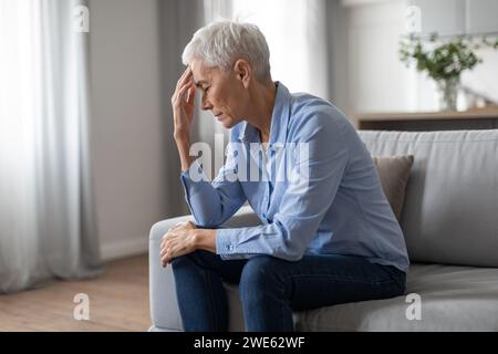 Depressive europäische Seniorin, die unter Kopfschmerzen leidet und drinnen den Kopf berührt Stockfoto