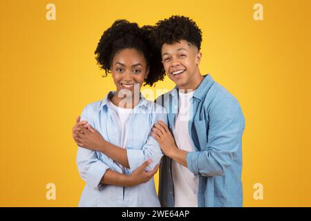 Fröhliches junges Paar aus stylischem Denim, das mit einem hellen Lächeln hinten an hinten steht Stockfoto