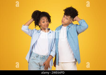 Afroamerikanischer Bruder und Schwester in lässigen blauen Hemden posieren mit Händen auf dem Kopf Stockfoto