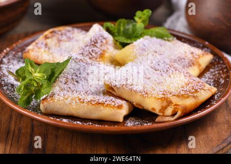 Dünne Pfannkuchen gefüllt mit Hüttenkäse, Honig und Rosinen, in einen Umschlag gewickelt, mit Puderzucker bestreut, garniert mit Minze. Festliches Gericht Stockfoto