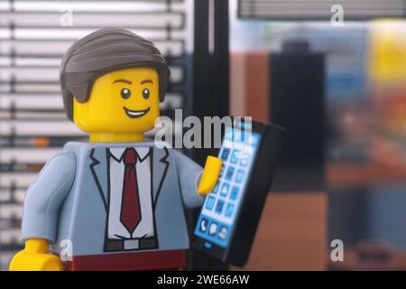 Tambow, Russische Föderation - 23. Januar 2024 Eine Lego-Geschäftsmann-Minifigur, die vor einem Bürofenster steht und das Handy entgegennimmt. Stockfoto