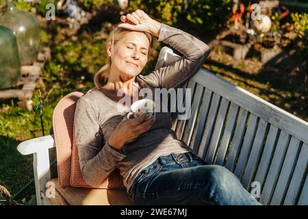 Frau mit Tasse Kaffee entspannt auf Gartenbank Stockfoto