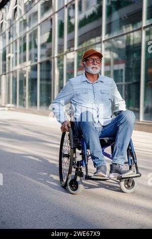 Pensionierter Seniorenmann, der im Rollstuhl auf dem Fußweg sitzt Stockfoto