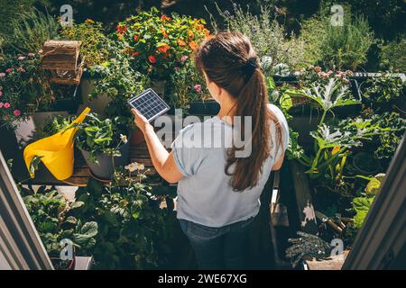 Frau, die Solarbatterie in der Nähe von Pflanzen auf dem Balkon hält Stockfoto