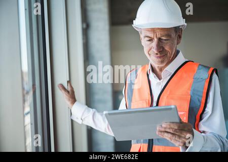 Lächelnder Senior Engineer mit Tablet-PC in der Nähe des Fensters Stockfoto