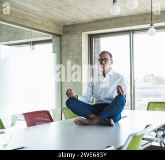 Geschäftsmann mit geschlossenen Augen und Meditation auf dem Schreibtisch im Büro Stockfoto