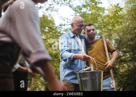 Senior-Mann, der eine Person mit Down-Syndrom bei der Teilnahme an der kommunalen Säuberung im Park unterstützt Stockfoto