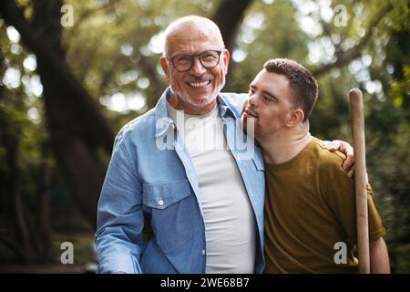 Senior-Mann, der eine Person mit Down-Syndrom bei der Teilnahme an der kommunalen Säuberung im Park unterstützt Stockfoto