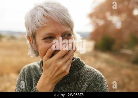 Glückliche Frau mit grauen Haaren, die den Mund bedeckt und lacht Stockfoto