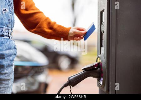 Frau, die mit Kreditkarte an der Ladestation für Elektroautos bezahlt Stockfoto