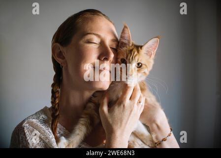 Frau mit geschlossenen Augen, die Katze zu Hause umschließt Stockfoto