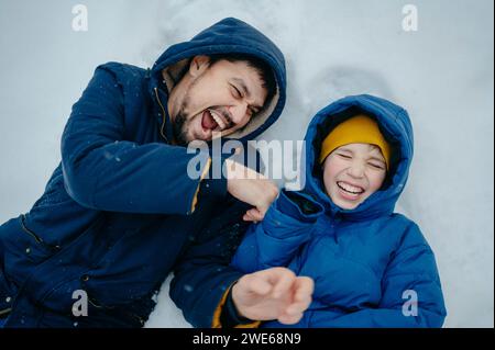 Glücklicher Vater mit Sohn, der auf Schnee liegt und im Winter lacht Stockfoto