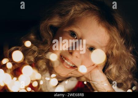Lächelndes blondes Mädchen, das durch Lichterketten schaut Stockfoto