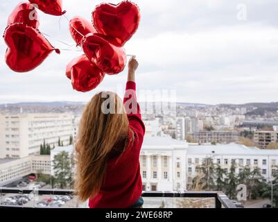 Rothaarige Frau, die rote Ballons auf dem Balkon hält Stockfoto