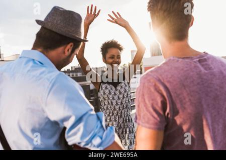 Lächelnde Frau tanzt und genießt mit Freunden auf dem Dach Stockfoto