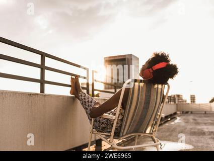 Frau, die Kopfhörer trägt und sich auf dem Dach entspannt Stockfoto