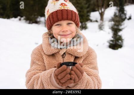 Lächelndes Mädchen, das Tee im Winterwald hält Stockfoto