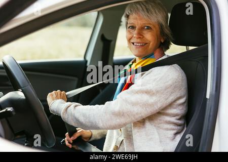 Lächelnde reife Frau, die im Auto den Sicherheitsgurt schnallt Stockfoto