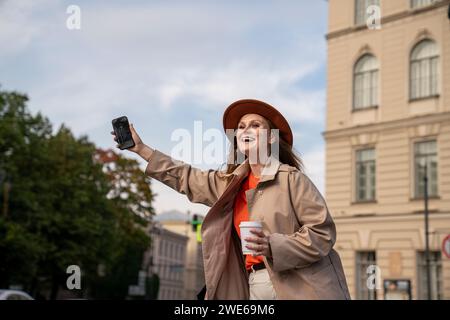 Glückliche Frau, die ihr Smartphone hält und in der Nähe des Gebäudes fährt Stockfoto
