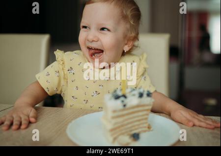 Glückliches Mädchen, das Geburtstag mit Kuchen am Tisch feiert Stockfoto
