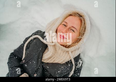 Glückliche junge Frau, die auf Schnee liegt Stockfoto