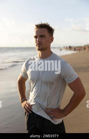 Junger Mann, der am Strand mit Händen auf Hüften steht Stockfoto