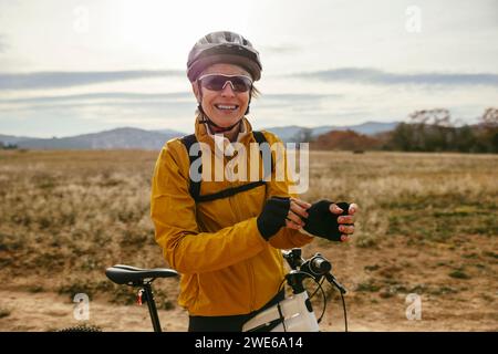 Lächelnde Frau, die Helm trägt und mit dem Mountainbike in der Nähe des Feldes steht Stockfoto