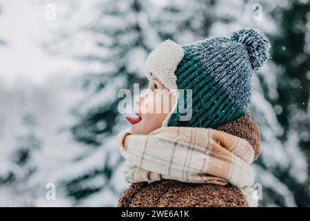 Süßer Junge, der im Winter mit der Zunge Schnee fängt Stockfoto