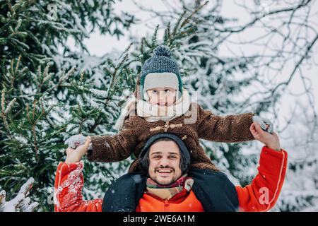 Glücklicher Mann, der den Sohn auf Schultern trägt und die Hände nahe am Baum hält Stockfoto