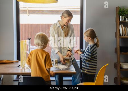 Glückliche Familie, die Teig zu Hause in der Nudelmaschine schneidet Stockfoto