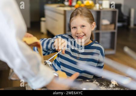 Glückliches Mädchen mit Mutter, die Teig im Teigmacher schneidet Stockfoto