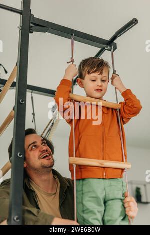 Der lächelnde Vater bringt dem Sohn bei, zu Hause auf eine Seilleiter zu klettern Stockfoto