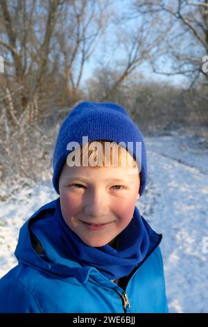 Lächelnder Junge mit Strickmütze im Winterwald Stockfoto