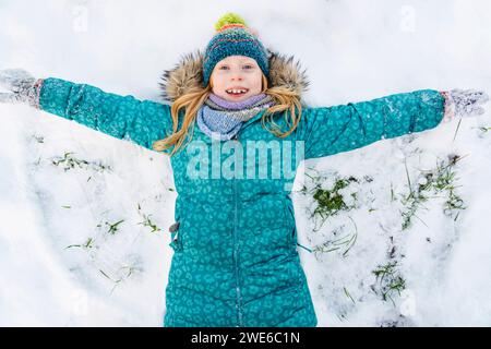 Ein verspieltes Mädchen, das eine Parkajacke trägt und einen Schneeengel macht Stockfoto