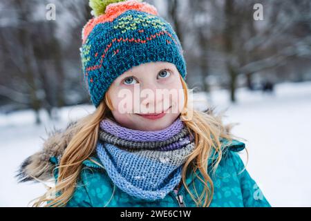 Lächelndes blondes Mädchen mit Schal und Strickmütze im Winter Stockfoto