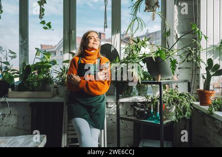 Lächelnder Botaniker mit geschlossenen Augen auf Fensterbank im Fabrikgeschäft Stockfoto
