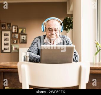 Senior-Mann mit Kopfhörern und Laptop zu Hause Stockfoto