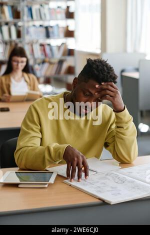 Müde Studentin mit Kopf in Hand, die Buch in der Bibliothek liest Stockfoto