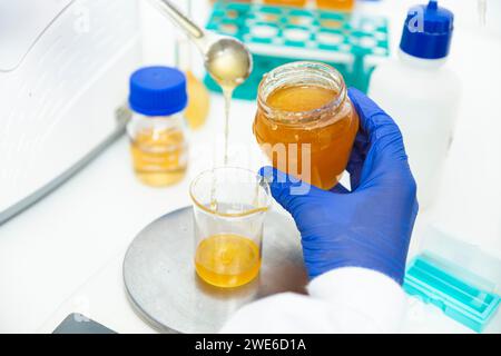 Hand des Wissenschaftlers, der Honig im Messbecher im Labor abwägt Stockfoto