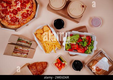 Fastfood und Gemüsesalat in der Nähe von Kaffeetassen vor beigem Hintergrund Stockfoto