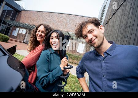 Glückliche multirassische Freunde stehen am Elektroauto Stockfoto